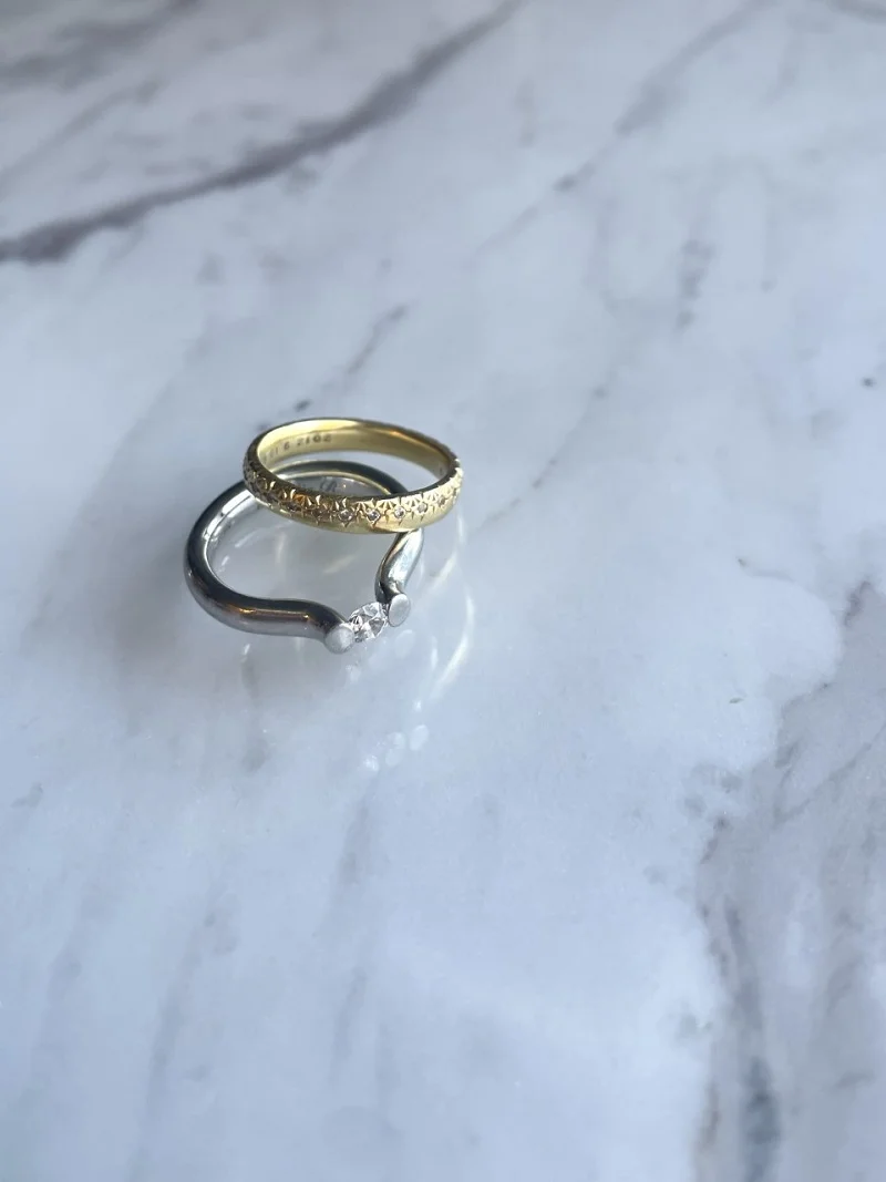 アーティスティックな佇まいが印象的なニーシングのエンゲージメントリング。手作業で彫られた模様が美しいハムのマリッジリングは重ね着けを想定してセレクト